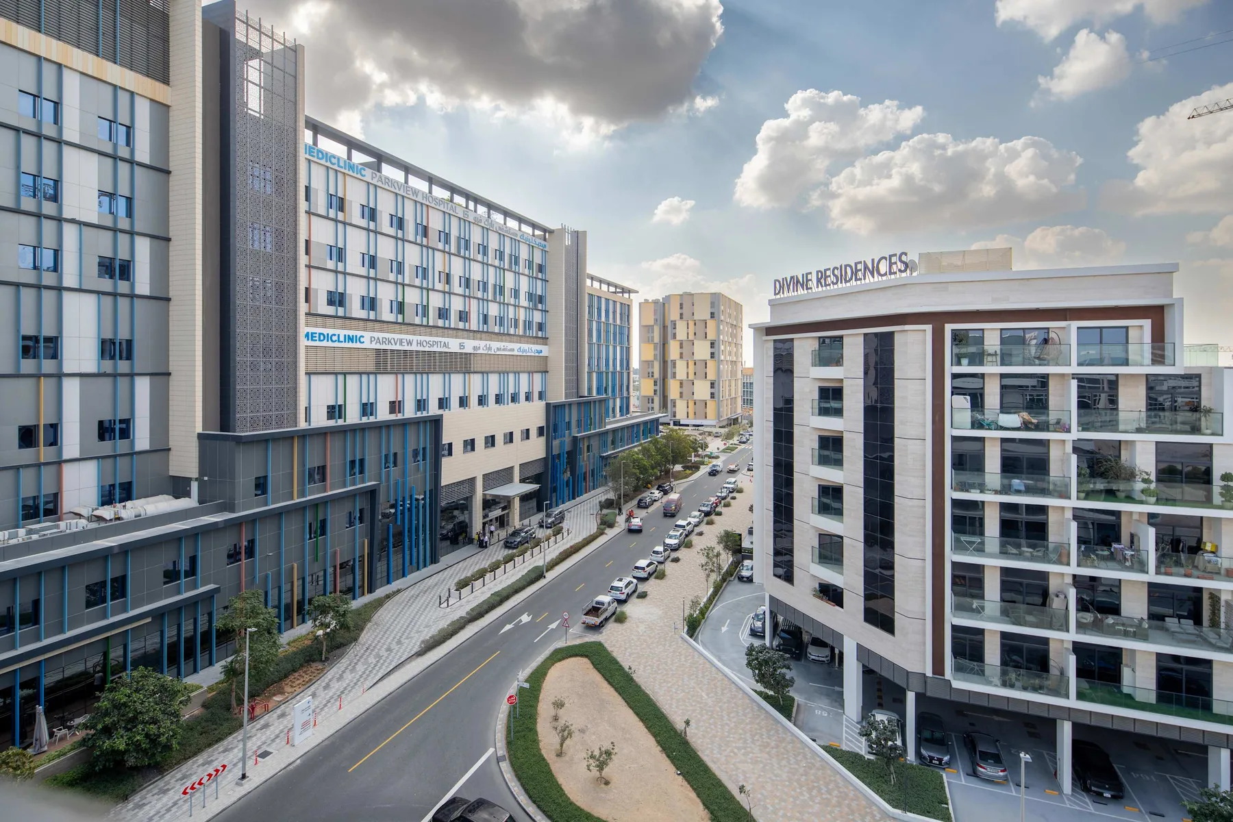 Modern residential buildings line a city street beneath a partly cloudy sky.