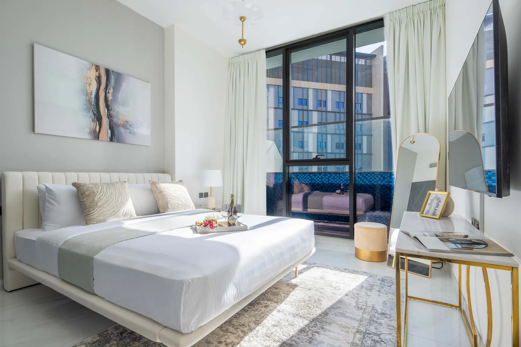 A bright bedroom with a neatly made bed beside floor-to-ceiling windows.