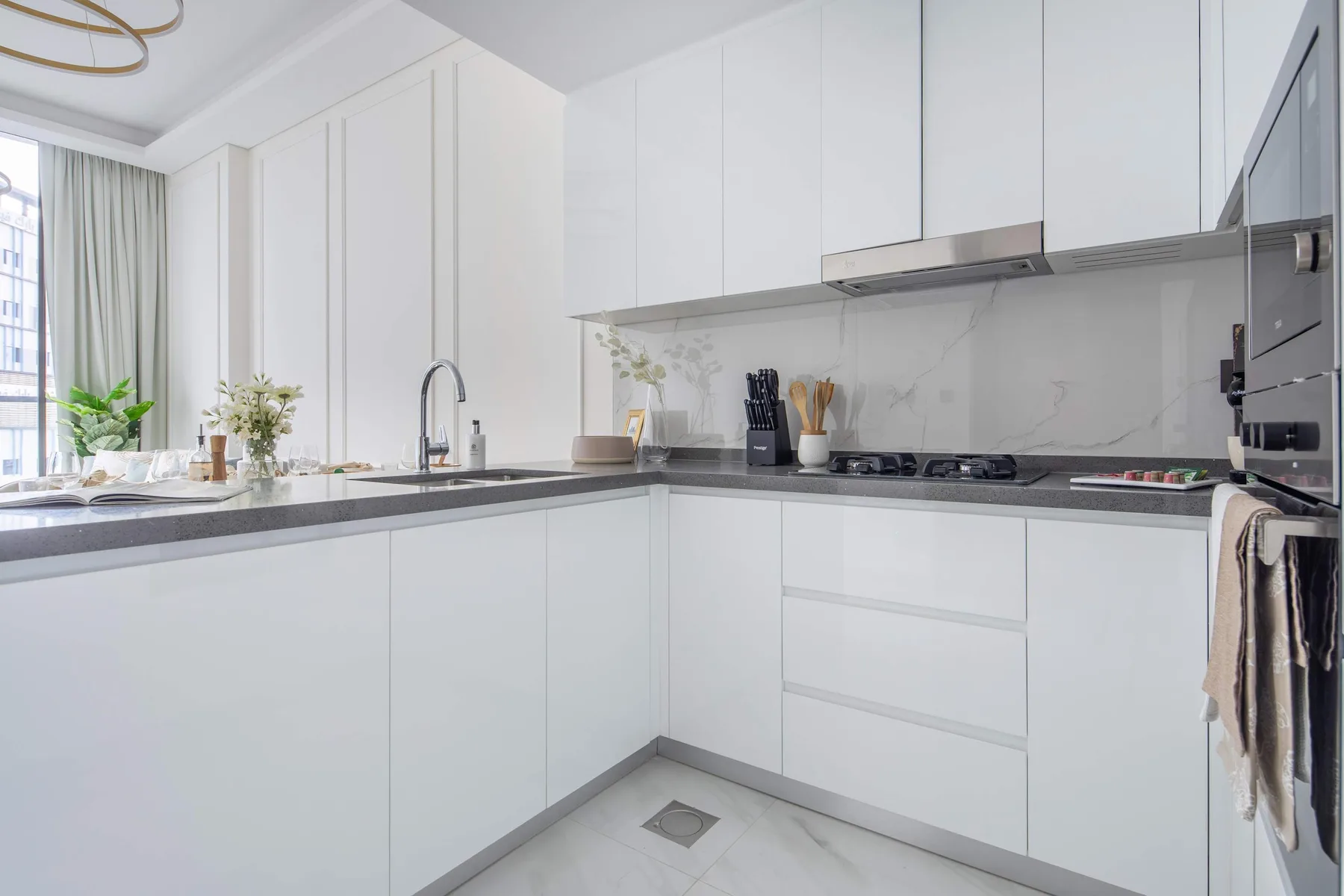 A bright white kitchen with a long counter, cooktop, and built-in oven.