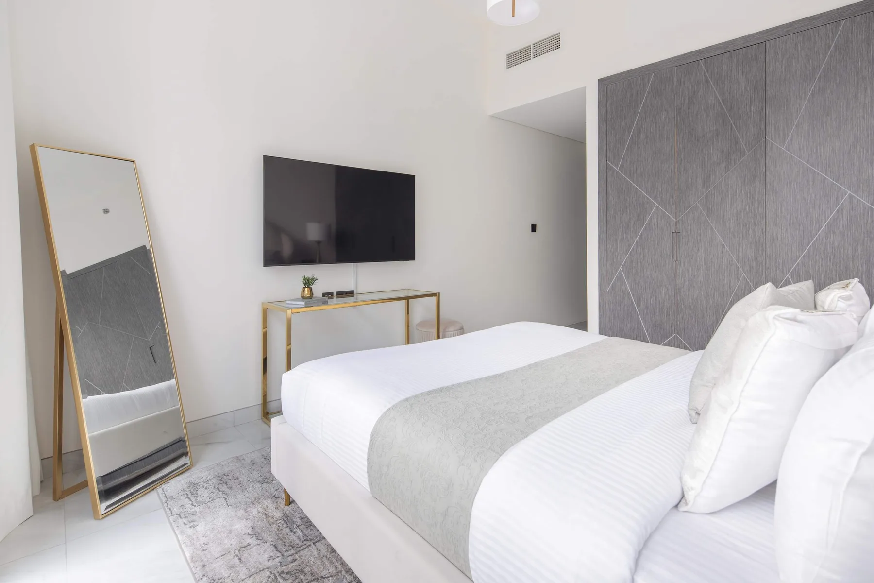 A bright bedroom with a bed, wall-mounted television, and full-length mirror.