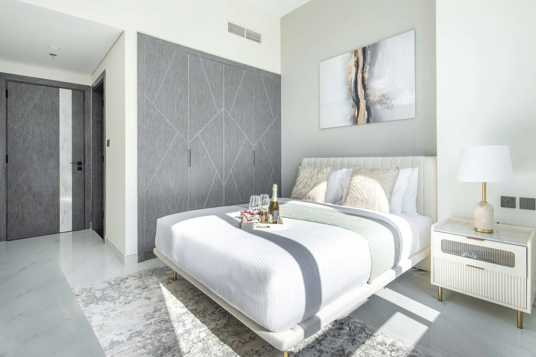 A bright bedroom with a neatly made bed and abstract artwork above the headboard.