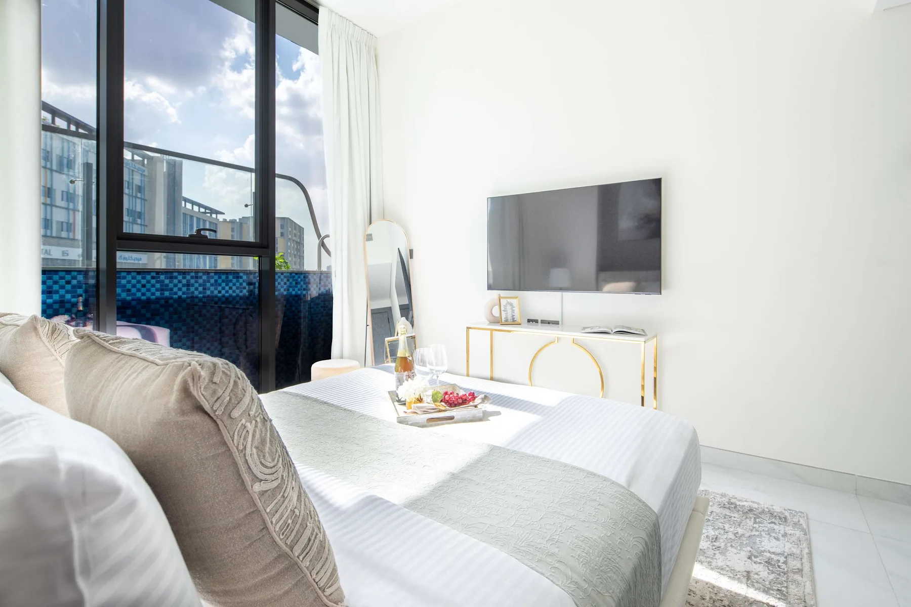 A bright bedroom with a bed beside large windows and a wall-mounted television.