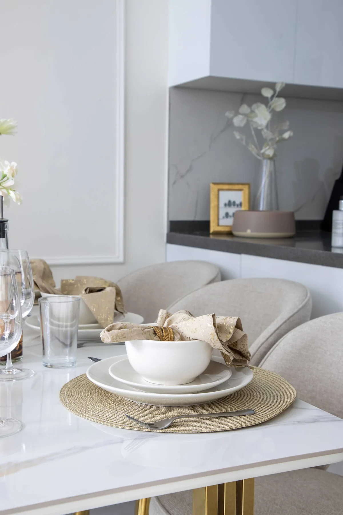 A dining table is set with dishes and woven placemats beside upholstered seating.