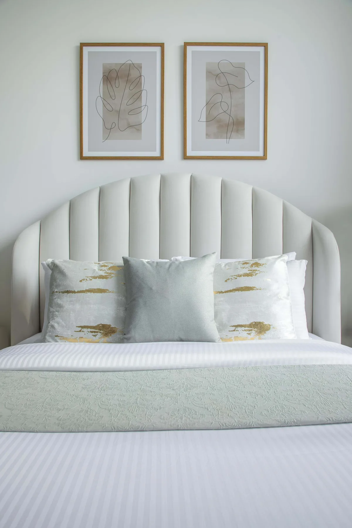 A neatly made bed with a curved upholstered headboard and framed artwork above.