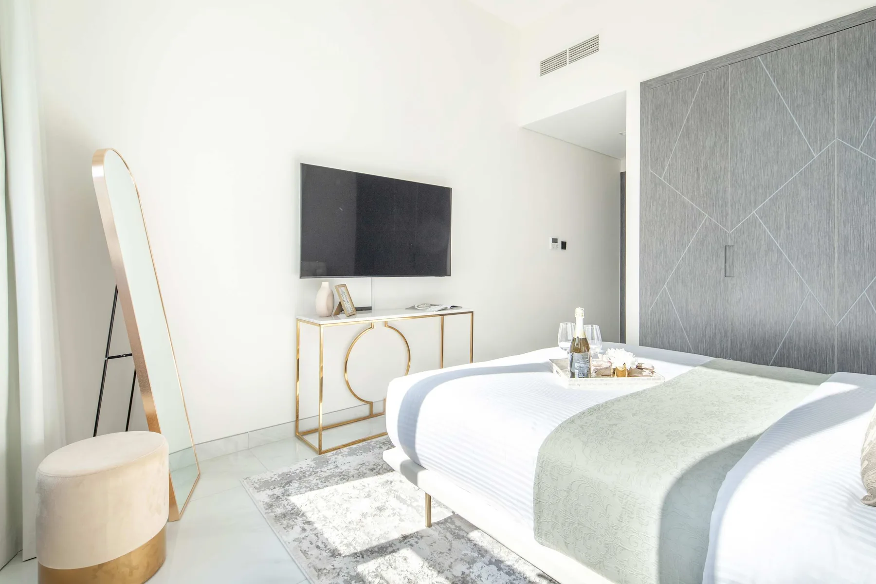 A bright bedroom with a neatly made bed and a wall-mounted television.