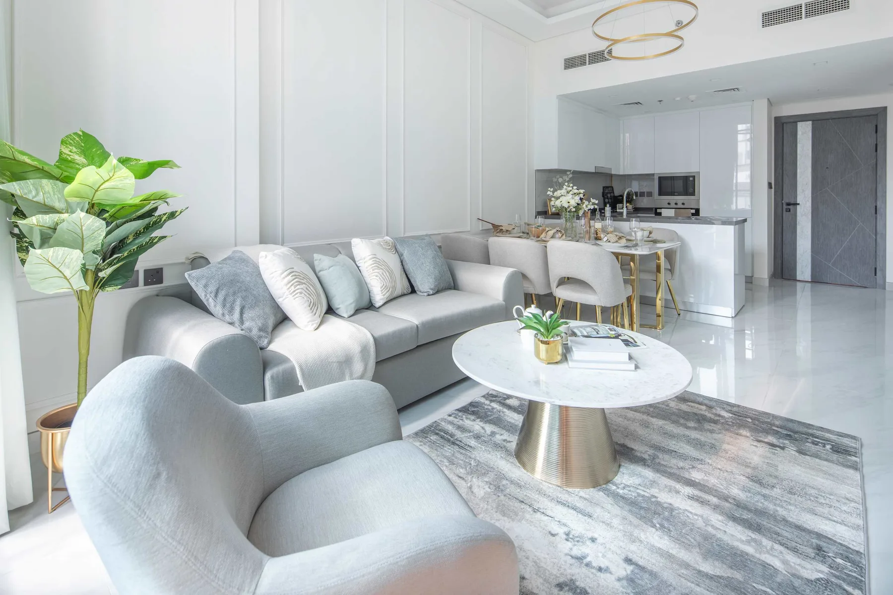 A bright living room with pale seating, a round coffee table, and an open kitchen.