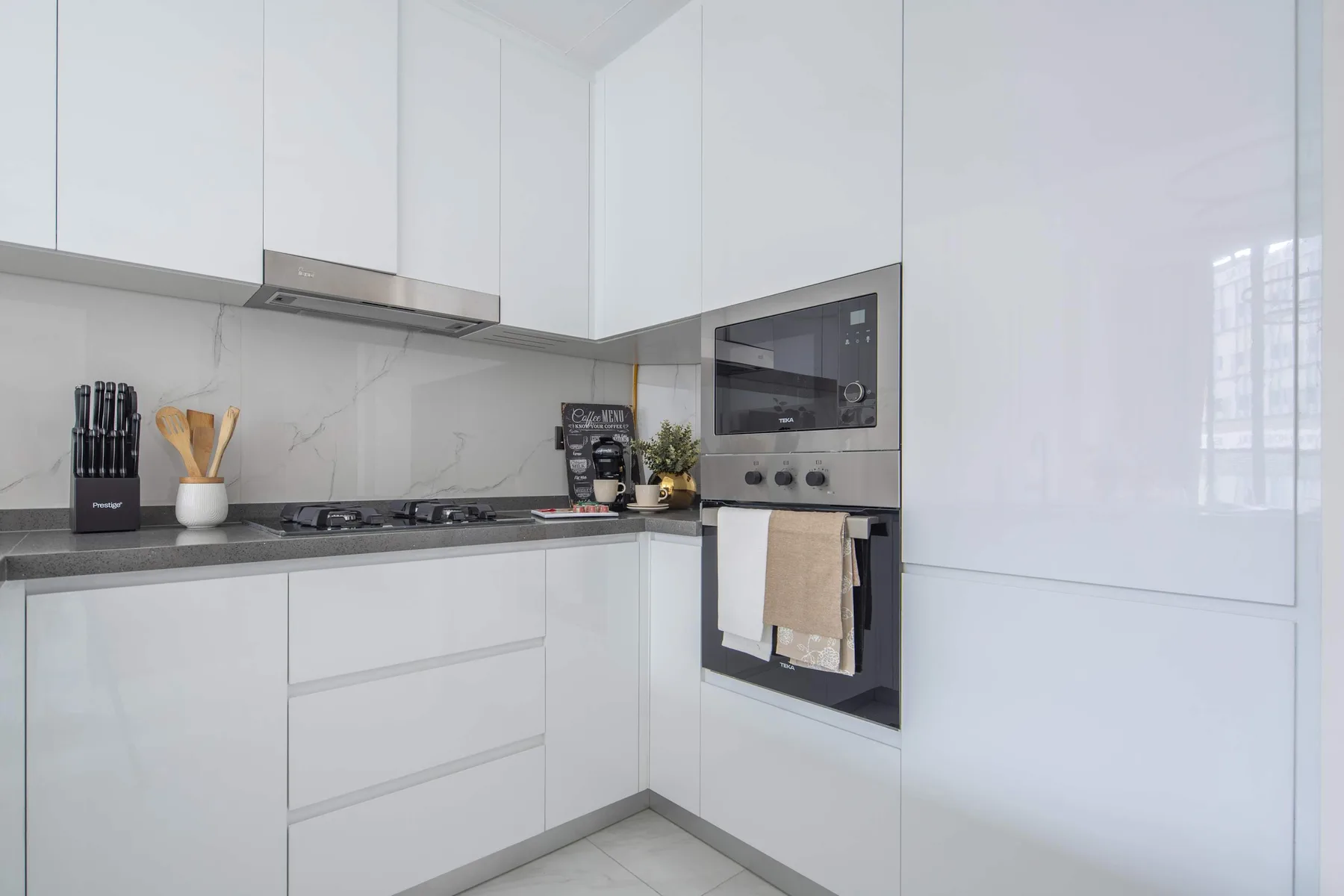 A bright modern kitchen with white cabinetry and built-in cooking appliances.