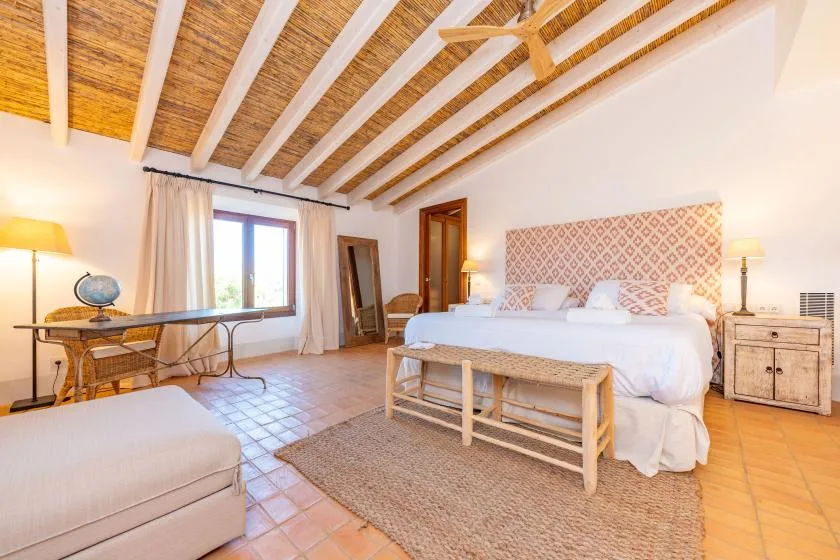 Un dormitorio con una cama grande, un escritorio y vigas de techo expuestas.