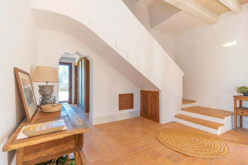 Una habitación luminosa con suelo de baldosas y una mesa de madera bajo una escalera inclinada.