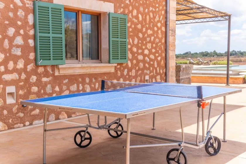 Una mesa de tenis de mesa está junto a una pared de piedra y una ventana.
