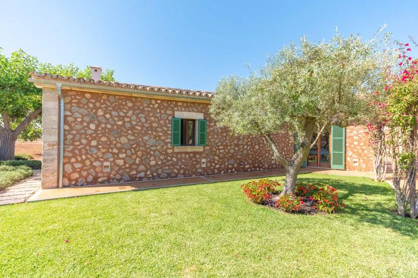 Una casa de piedra se alza junto a un césped verde y un jardín florido.