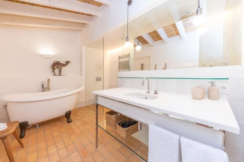 Un baño luminoso con bañera, una amplia encimera con lavabo y vigas expuestas.