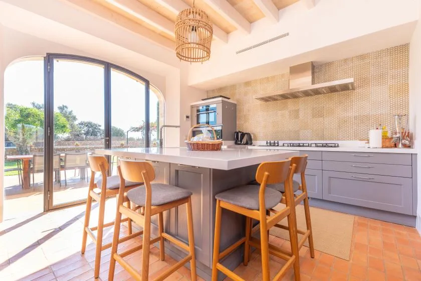 Una cocina luminosa con una isla central y asientos junto a grandes ventanas arqueadas.
