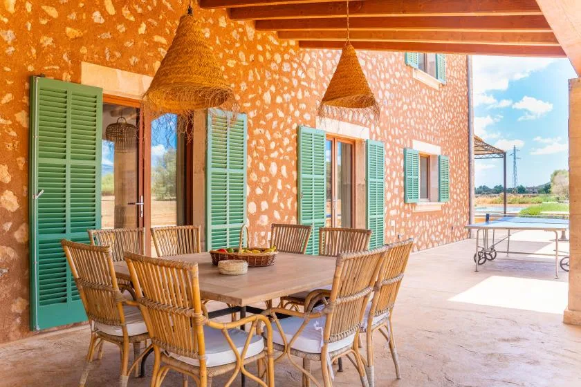 Un comedor exterior cubierto con una mesa larga y asientos tejidos.