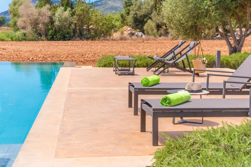 Una terraza junto a la piscina con asientos reclinables y toallas verdes.