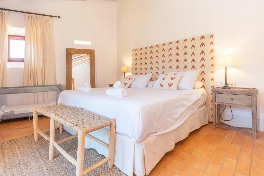 Un dormitorio con una cama grande, un cabecero estampado y un banco tejido.