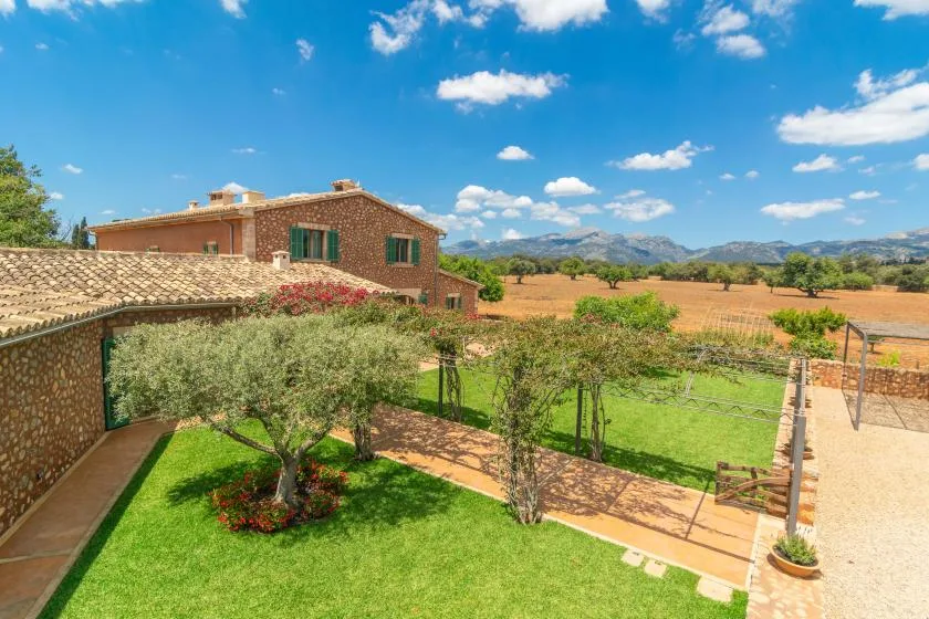 Un jardín con césped y árboles da a una casa de ladrillo y al campo abierto.