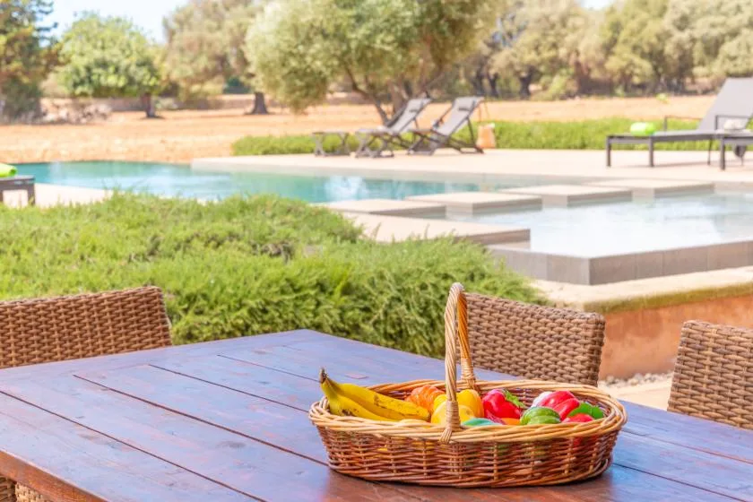 Comedor al aire libre con una cesta de frutas junto a una piscina.