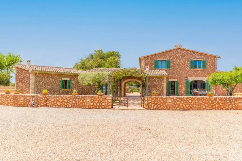 Una casa de ladrillo se alza tras un muro bajo de piedra, con una entrada arqueada.