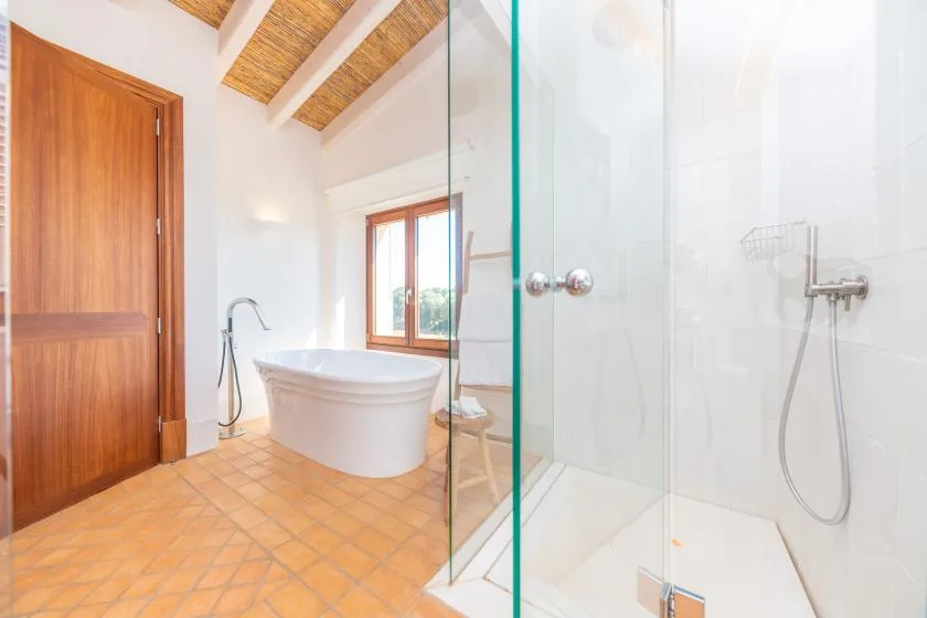 Un baño luminoso con bañera, ducha de vidrio y vigas expuestas en el techo.