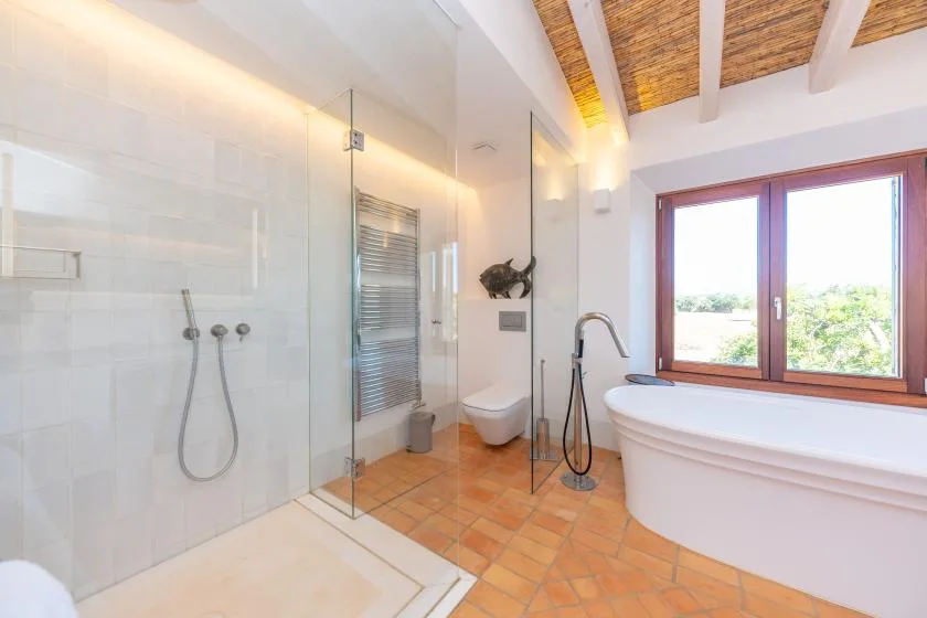 Un baño luminoso con ducha de vidrio, bañera y una ventana grande.