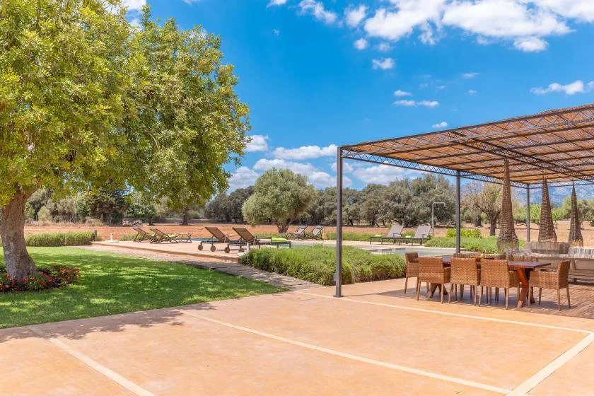 Un patio al aire libre con asientos a la sombra, jardines y árboles.