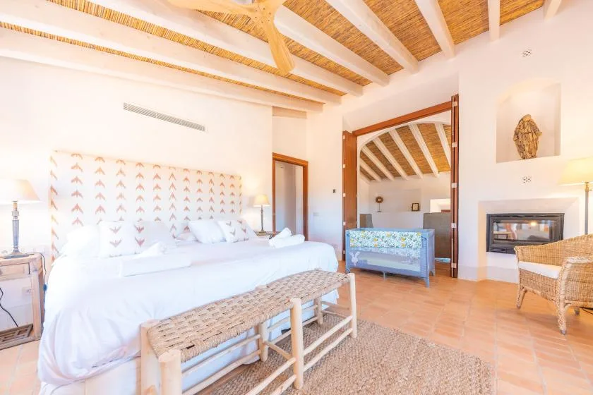 Un dormitorio luminoso con una cama grande, un banco tejido y vigas de madera expuestas en el techo.