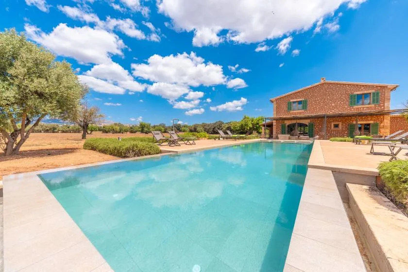 Una piscina al aire libre junto a una casa de ladrillo, con asientos y árboles.