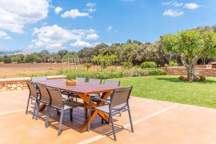 Una mesa de comedor y asientos al aire libre están en un patio junto a un césped verde.