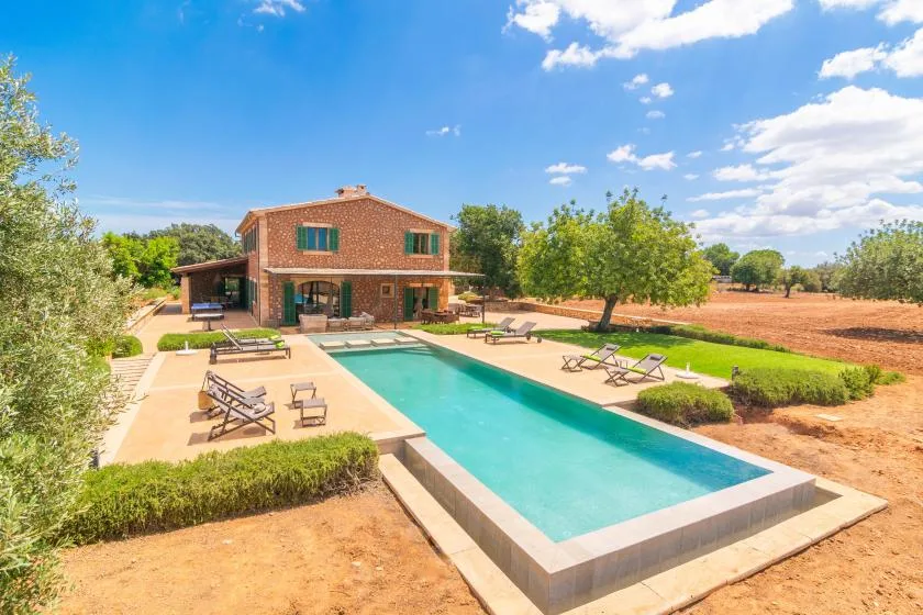 Una piscina junto a una casa de ladrillo, con asientos de descanso en el patio.