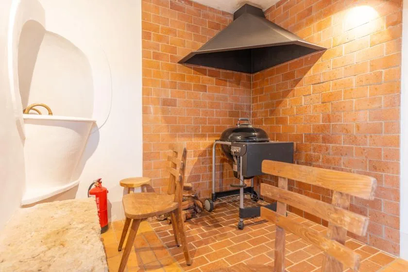 Una zona de cocina con paredes de ladrillo, una campana metálica grande y asientos de madera.