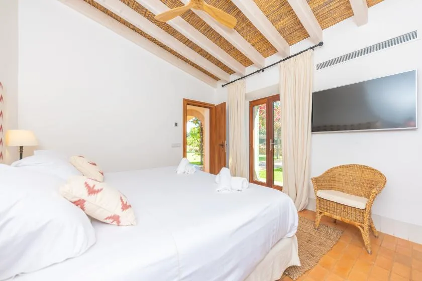 Un dormitorio con una cama grande, un televisor en la pared y una silla de mimbre.