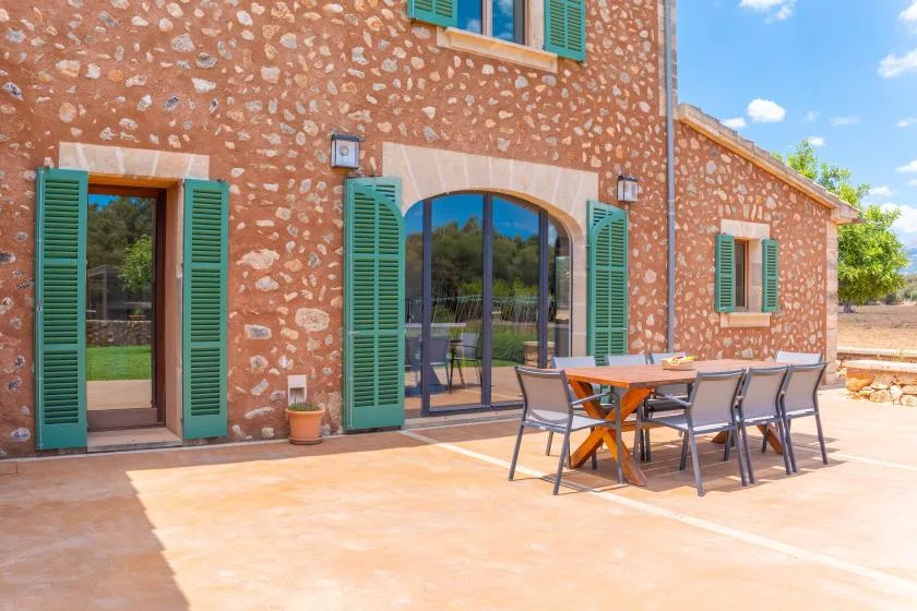 Un patio de una casa de piedra con persianas verdes y muebles de comedor al aire libre.
