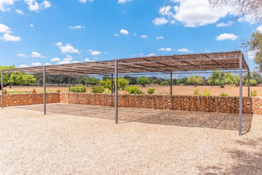 Un patio al aire libre con una pérgola sombreada y muros bajos de piedra.