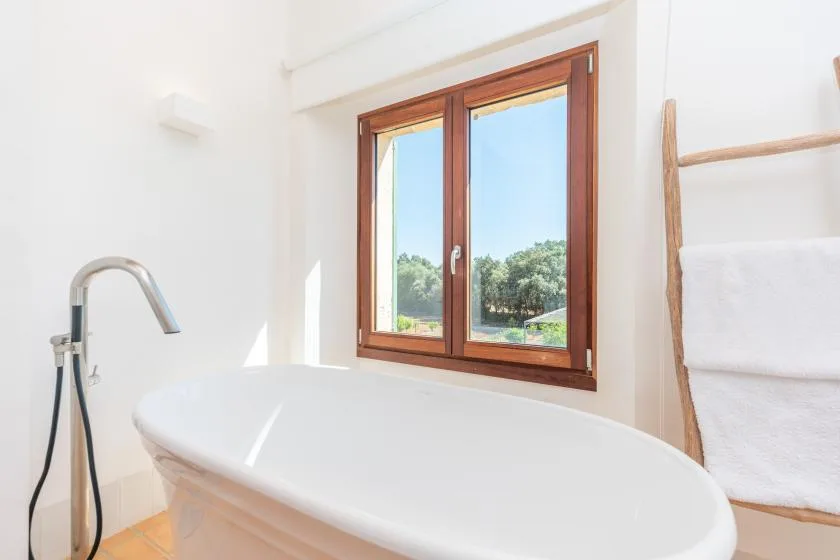 Un baño luminoso tiene una bañera exenta junto a una ventana con vistas a la vegetación.