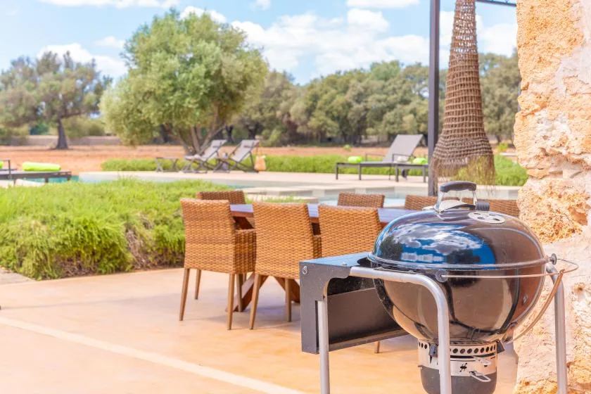 Comedor al aire libre con asientos de mimbre y una parrilla con tapa abovedada.