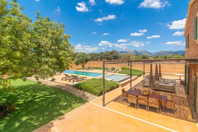 Un patio exterior da a una piscina, con una zona de comedor a la sombra.