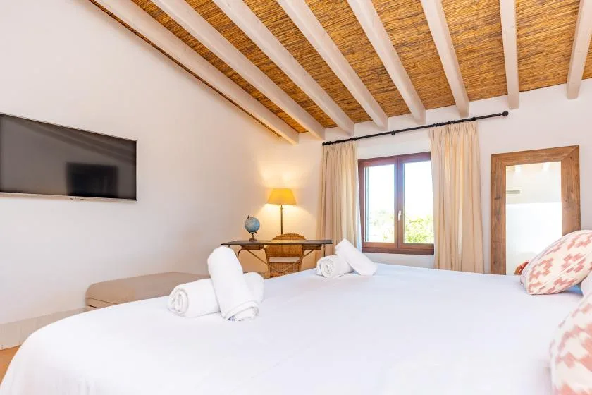Un dormitorio luminoso con una cama grande, una ventana y vigas vistas en el techo.