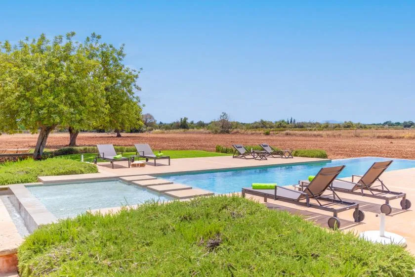Una piscina al aire libre con tumbonas está junto a un césped.