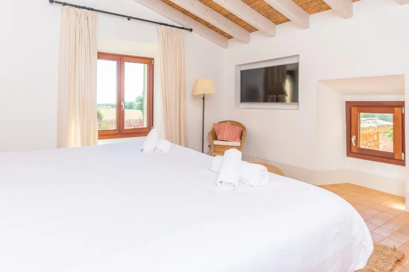Un dormitorio luminoso con una cama grande, ventanas con cortinas y vigas vistas en el techo.