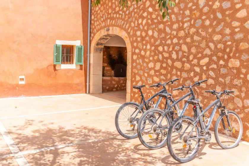 Hay bicicletas junto a una puerta arqueada en un patio soleado.