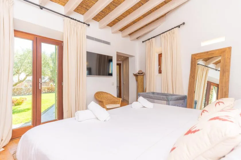Un dormitorio luminoso con una cama grande, un televisor en la pared y puertas acristaladas hacia el exterior.