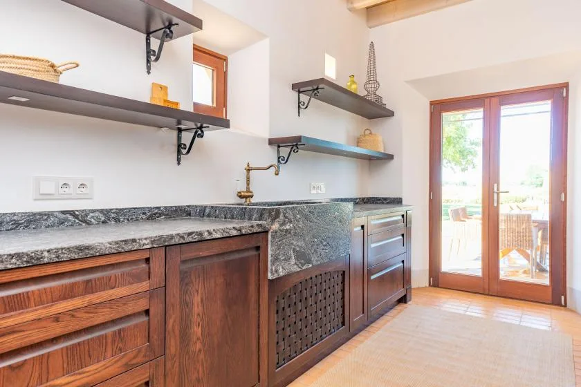 Una cocina luminosa con gabinetes de madera, encimeras de piedra y puertas de vidrio que dan a un patio.