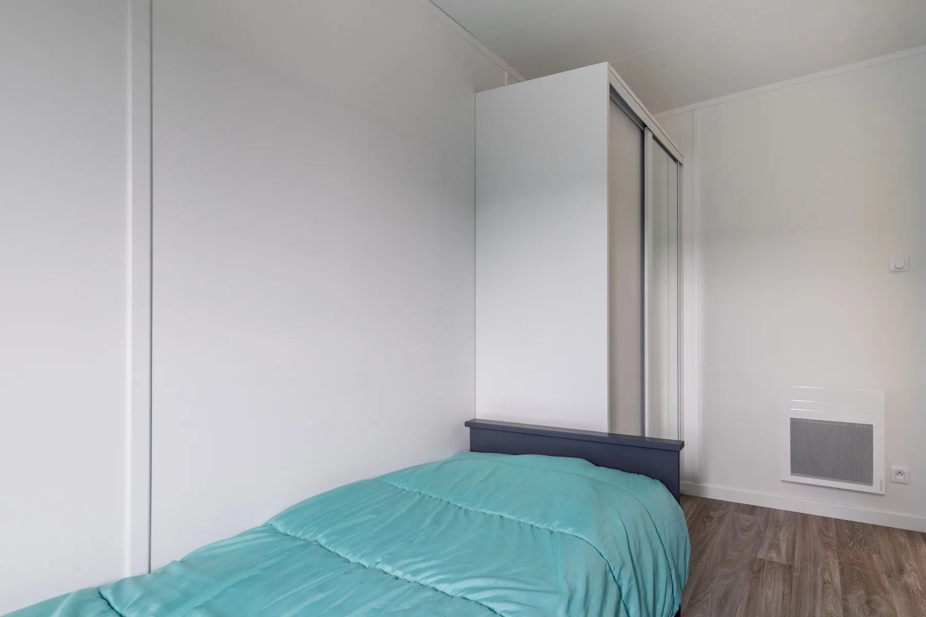A bedroom with a bed covered by a turquoise duvet.
