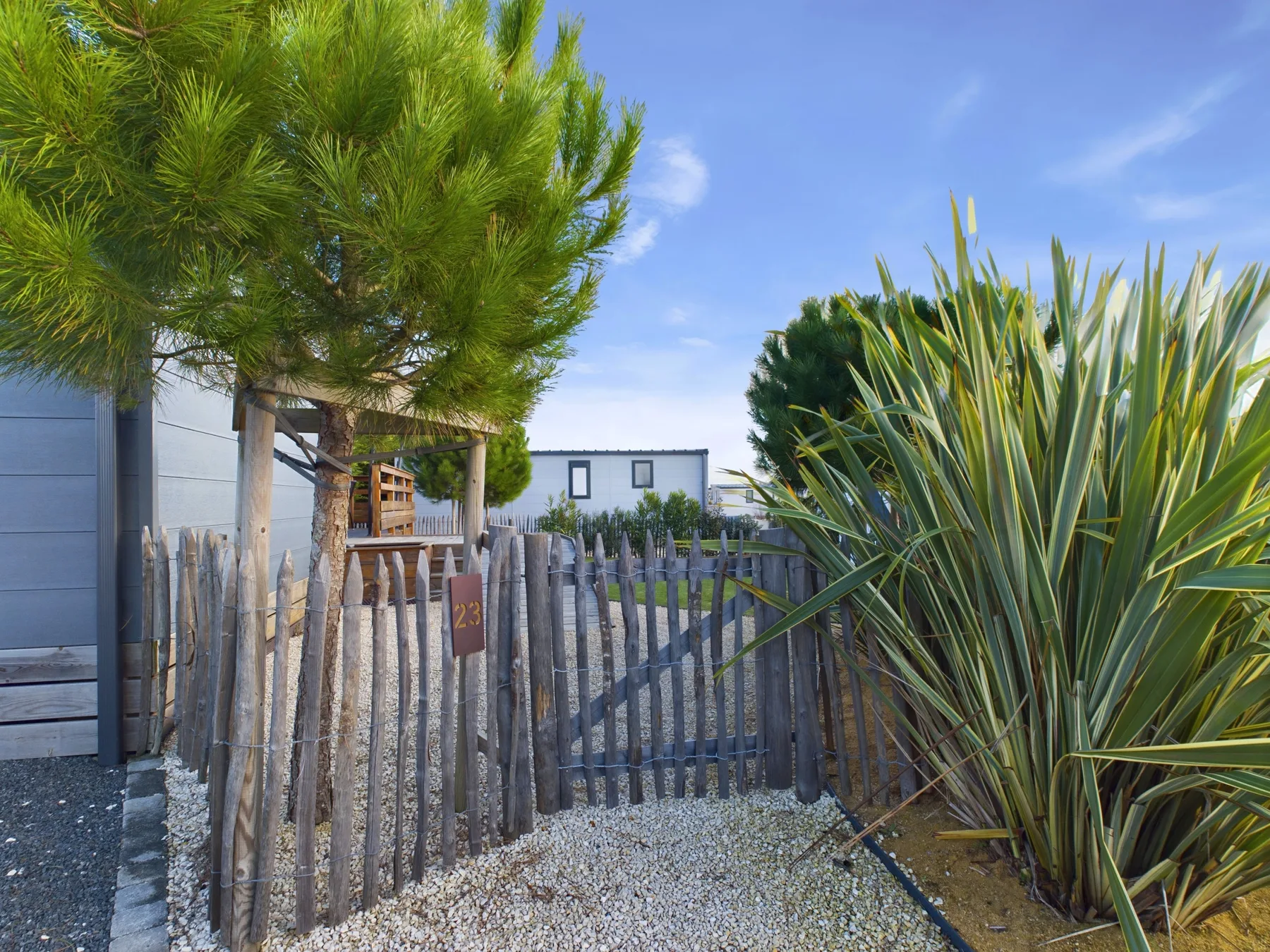 An outdoor entrance is bordered by a rustic wooden fence and leafy plants.