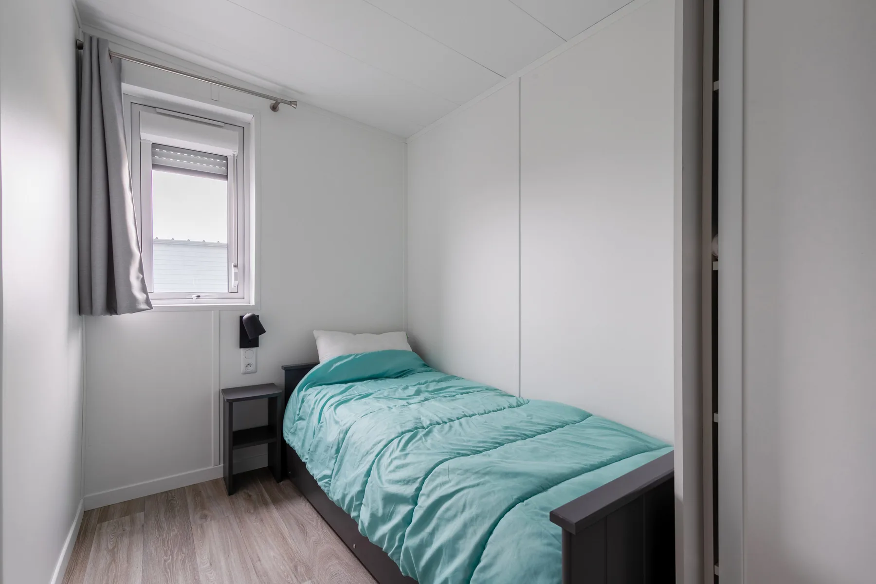 A bedroom with a single bed dressed in turquoise bedding.