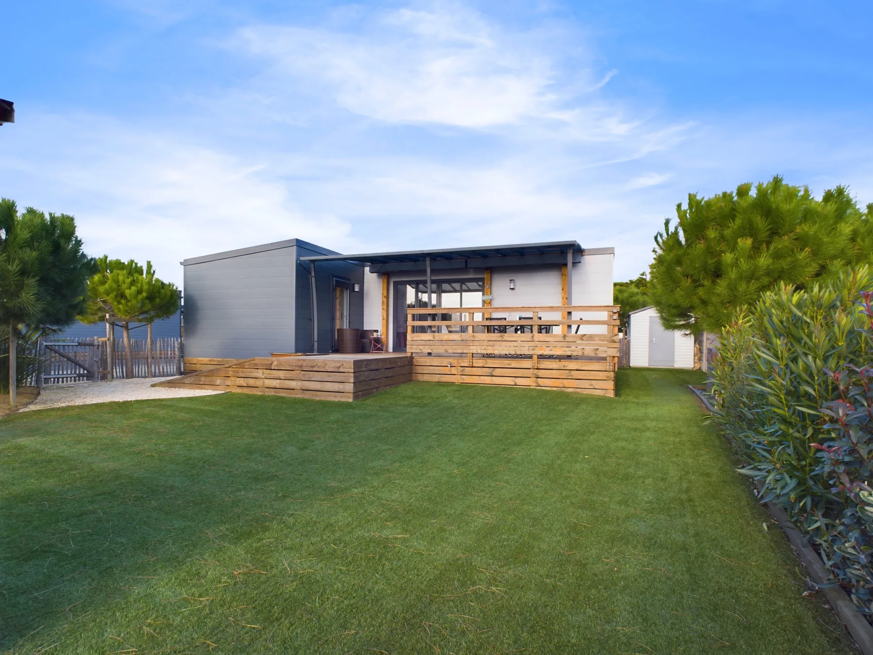 A modern house opens onto a wooden deck overlooking a green lawn.