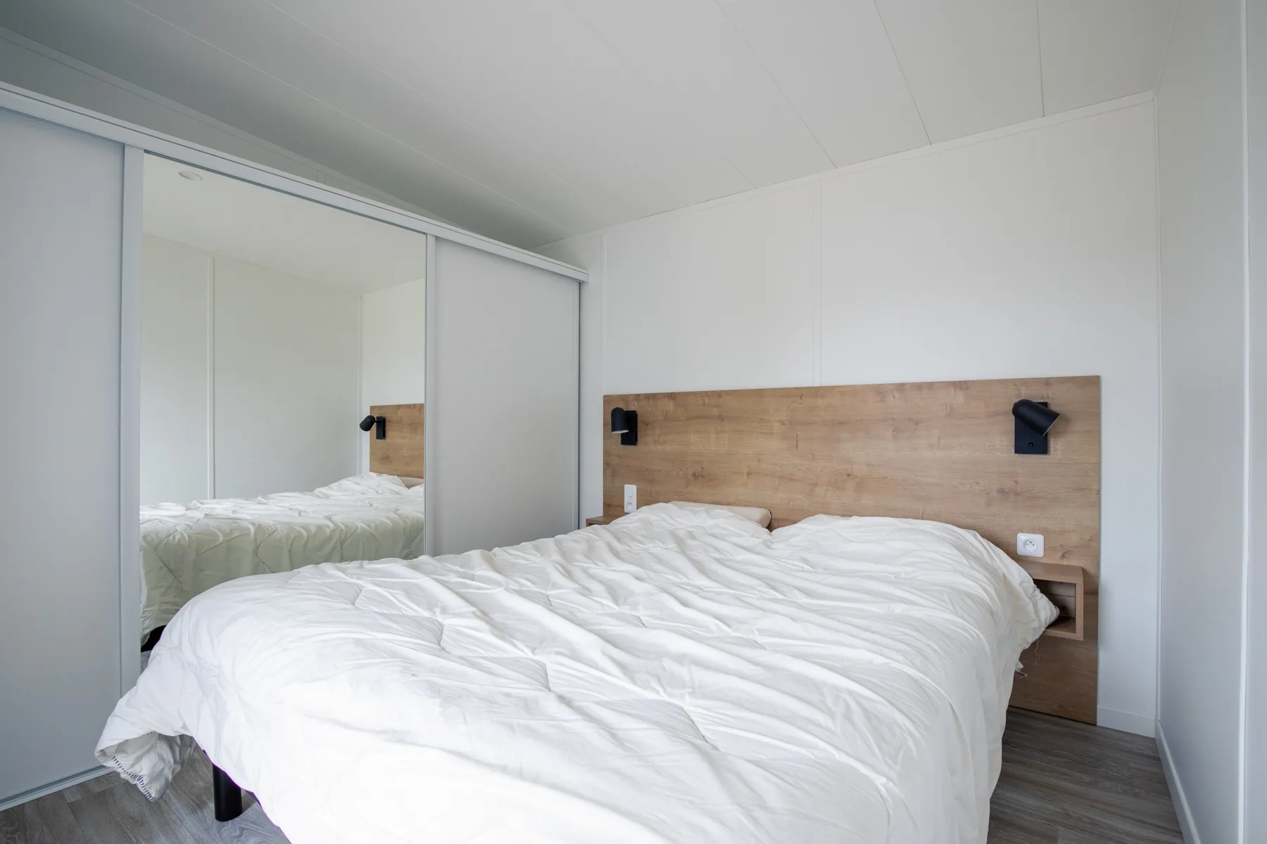 A bright bedroom with a bed and mirrored closet doors.