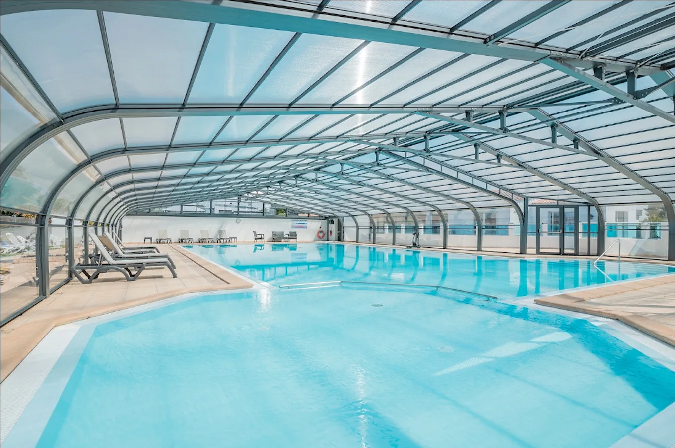 An indoor swimming pool beneath a transparent arched roof.