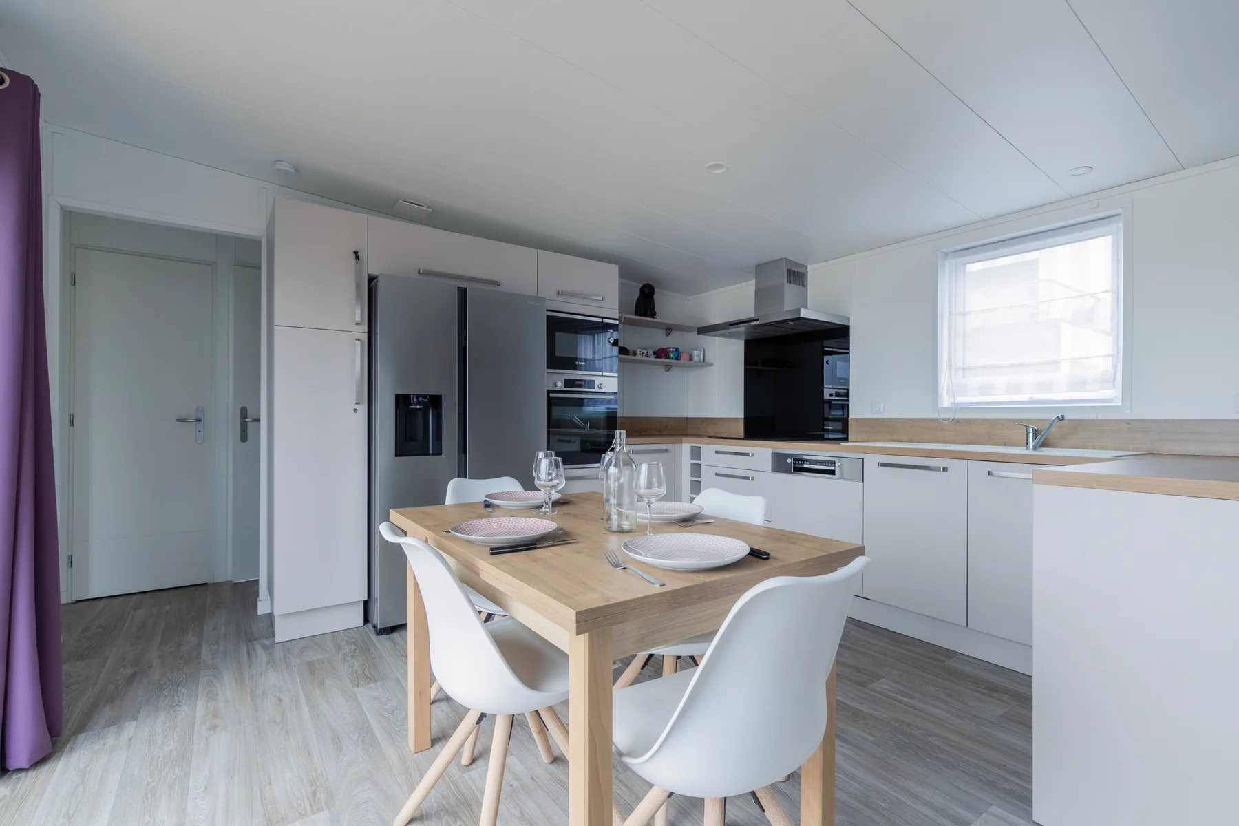 A bright kitchen with white cabinetry and a wooden dining table.
